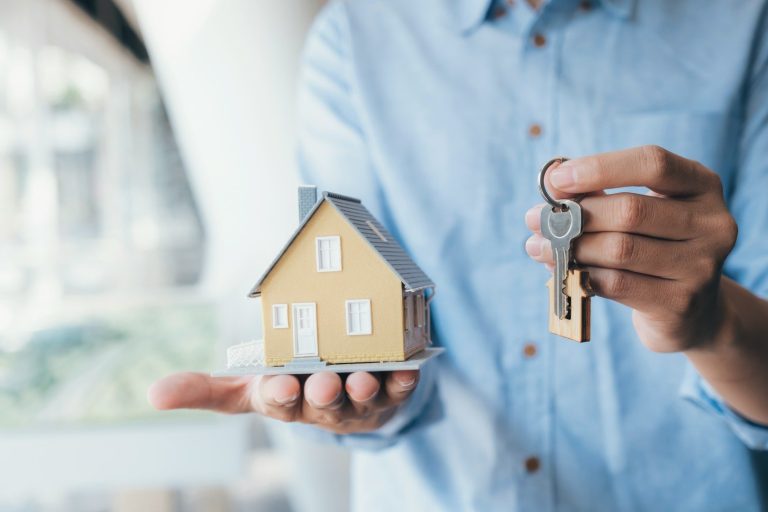 Eine Person hält ein kleines gelbes Hausmodell und Schlüssel in der Hand.