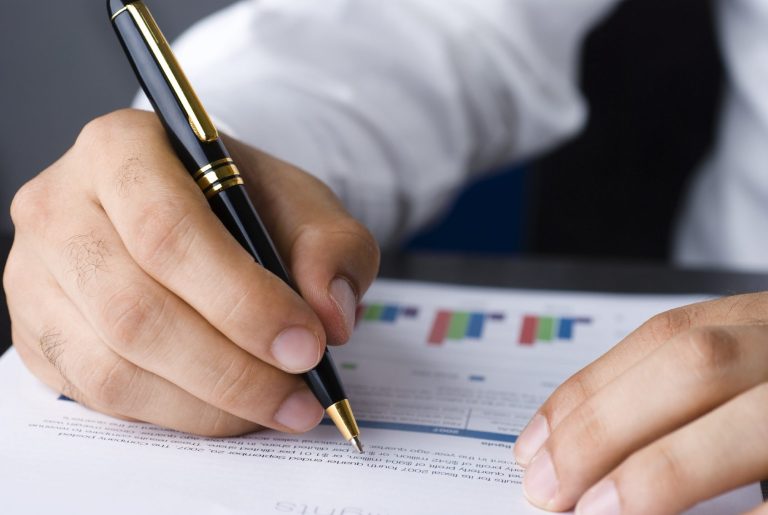 Eine Hand hält einen Stift über ein Dokument mit Diagrammen und Text.