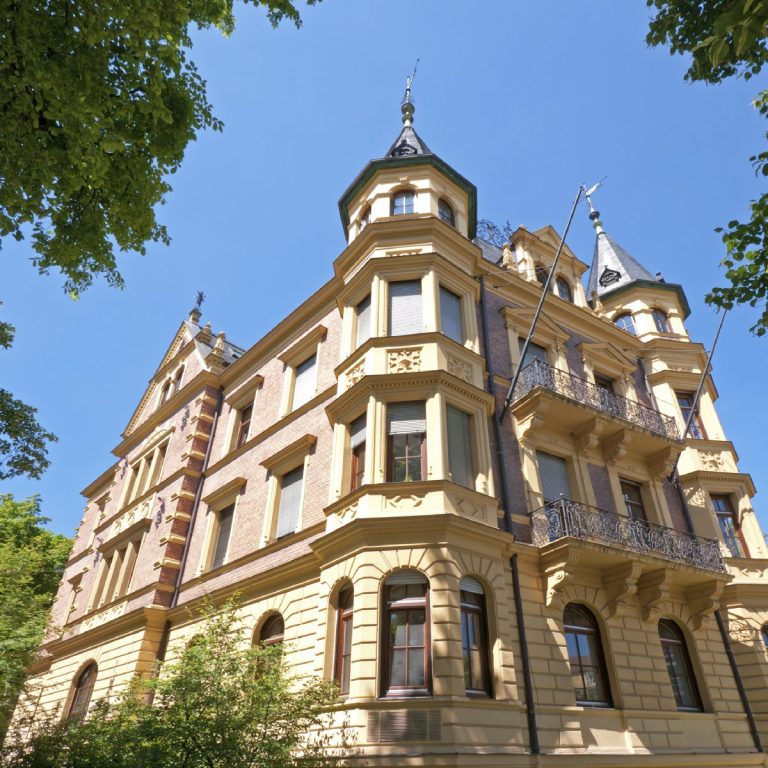 Historisches Gebäude mit Türmen und verzierten Fassaden unter klarem blauen Himmel.